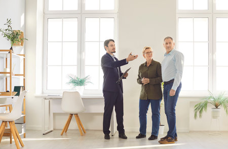 Realtor, real estate agent, broker represents senior sellers or buyer new property, clients during meeting looking at room, showing apartment, planning work, having discussion with engineer, architectの写真素材