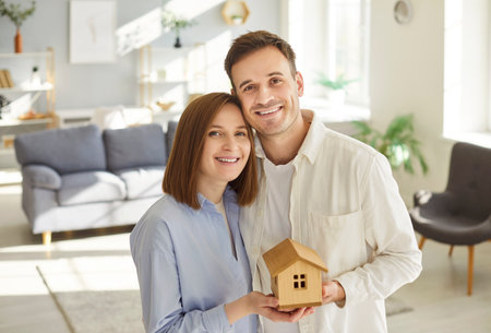 Happy smiling family holding new miniature wooden toy house, real estate dream, housing symbol, choosing home to buy, building, repair and renovation, mortgage, moving or renting property for lifeの写真素材
