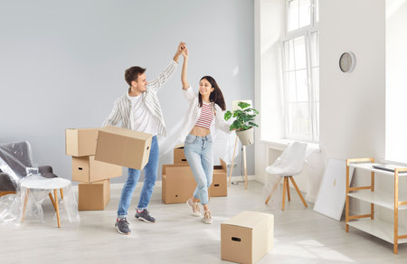 Excited homeowners, renters, happy to move new own flat, carrying boxes, married young couple enjoying moving into first house, man and woman couple feeling joy with relocation, dancing in joyの写真素材