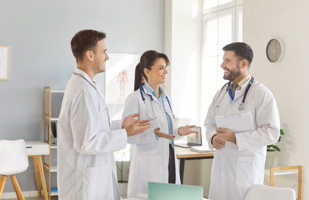 Team of happy professional doctors standing together in clinic, smiling and engaging in friendly conversation. Group of positive medical staff discussing their work, ideas, diagnosis or treatment.の写真素材