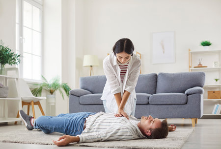 Young woman doing CPR on unconscious man lying on the floor at home. Wife trying to resuscitate her husband with heart attack or cardiac arrest indoors. First aid emergency concept.の写真素材