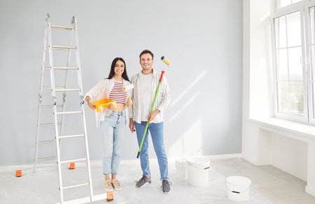 Portrait of a happy and cheerful couple standing together during the renovation of new home. Highlighting painting, construction, decorating, and the joy of creating a personal living space.の写真素材