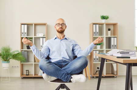 Calm serene office male employee sitting at chair in lotus pose relaxing doing yoga mudra, practice meditation to reduce stress, relief fatigue, feel balance workplace, improve mental health, thinkingの写真素材