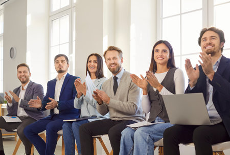 Crowd of business people gathers in the office, celebrating success with applause during a meeting or event. This moment highlights teamwork, diversity, and the joy of shared achievements.の写真素材