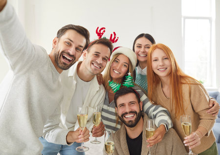 Portrait of young happy friends group standing in living room at home celebrating Christmas holiday or New Year and looking cheerful at camera making selfie with glasses of champagne in hands.の写真素材