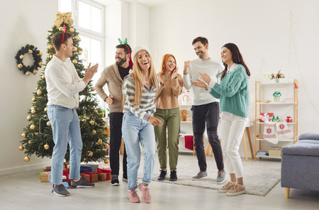 Happy smiling young people friends men and women having party, dancing in festive living room with decorated Christmas tree having fun celebrating New Year together. Winter holidays concept.の写真素材