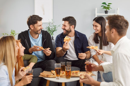 Friends eating pizza and drink alcohol during a fun party at home. Lively atmosphere brings laughter and enjoyment as they relax, eat, and drink together, creating moments of leisure and celebration.の写真素材
