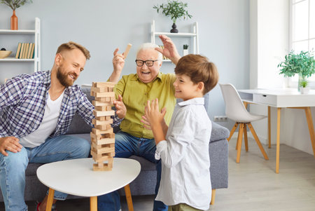 Overjoyed family of three generation men, senior grandfather, adult father, child grandson playing at home jenga board game together, making tower building, weekend celebrating fathers day holidayの写真素材