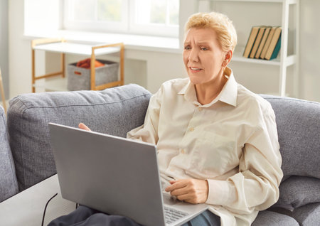Adult mature woman in difficult problem with work, freelancer working on computer at home, old businesswoman studying online, using laptop software, web surfing information or shopping in internetの写真素材