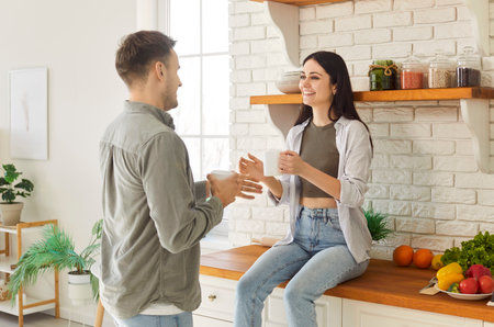 Happy friendly affectionate young married family couple enjoying talking in modern stylish kitchen, speaking spending carefree weekend leisure time in new own apartment, having morning drink, restingの写真素材