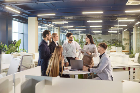 Group of coworkers or business people working together in an office, having a conversation and reviewing documents during a team meeting. Communication, teamwork, and professional engagement.の写真素材