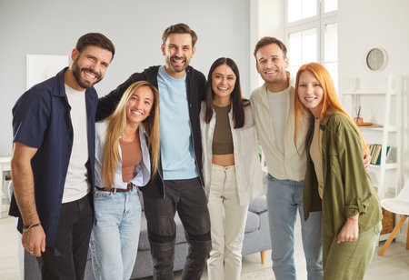 Group portrait of five happy smiling young supportive friends, students or colleagues standing together in row and hugging each other. Joyful group of people looking at camera and making group photo.の写真素材