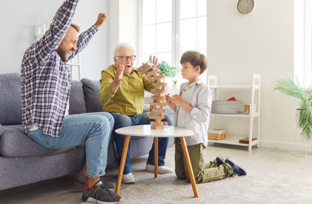 Happy family of three generation men, grandfather, father, son, cute child grandson playing at home jenga board game together, making tower building, enjoy weekend, celebrating fathers day holidayの写真素材