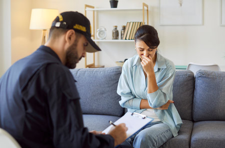 Police officer in uniform talking to robbery victim after burglary at home. Policeman making interview and interrogating young crying upset woman. Crime, robbery, safety of property concept.の写真素材