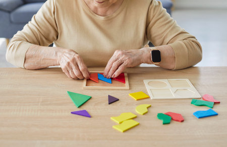 Cropped shot of attentive elderly woman assembling colourful geometric shapes, developing her motor...