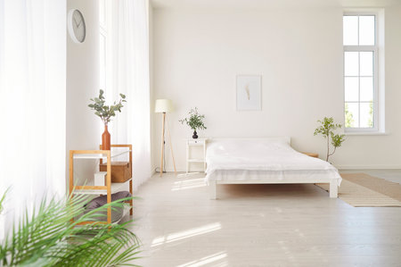 Empty, cozy bedroom with a comfortable white bed in a house or home. The peaceful interior creates a sense of comfort and warmth in the home during a quiet morning, inviting relaxation and rest.の写真素材