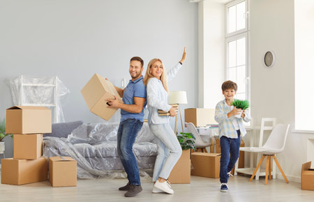 Happy family with child boy on moving day having fun with unpacked boxes and plant in hands in their...