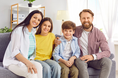 Smiling young happy family of four with two kids boy and girl sitting on the sofa at home and...