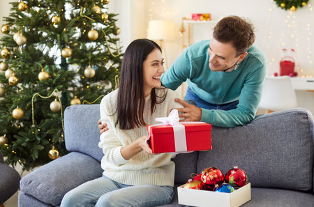Married couple enjoys opening presents during Christmas or New Year celebrations at home. The family cherishes the holiday moments, sharing gift boxes and joyful memories in a festive atmosphere.の写真素材