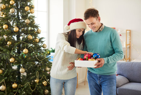 Husband and wife decorate family tree for Christmas or New Year at home. They select ornaments, enjoying leisure time together as they prepare for the holiday season with festive decorations.の写真素材
