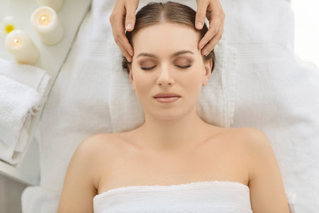 Top view of masseur hands making face relaxing massage to a young girl lying with closed eyes in beauty salon or cosmetology cabinet. Professional cosmetologist making massage for woman in spa.の写真素材