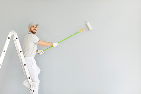 Portrait of a smiling painter or handyman holding a brush while painting walls during a renovation. Highlighting a professional approach to construction, repair, and decorative improvements.の写真素材