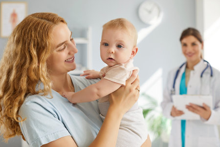 Portrait of happy smiling young mother with infant toddler cute little child baby visiting female friendly pediatrician doctor for medical examination standing in clinic. Health care concept.の写真素材