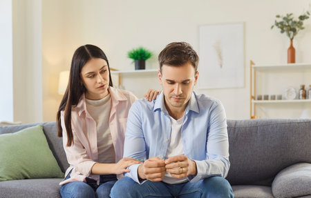Married couple engages in conversation at home, with wife offering support to sad husband, addressing depression and nurturing family relationship through open communication in a domestic comfort.の写真素材