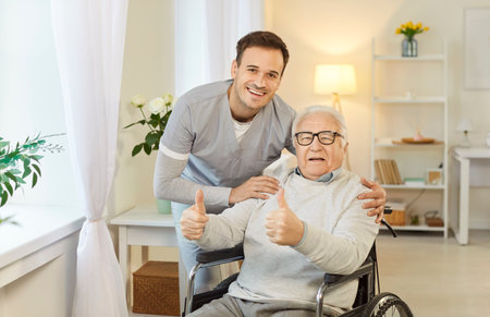 Positive health care worker embraces old male patient in wheelchair who shows thumb up gestures, encourages and says everything is fine, has big hope for recovery. Elderly people assistanceの写真素材
