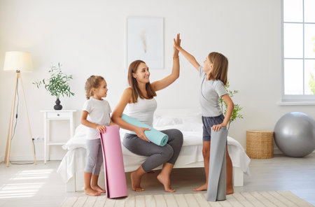 Mother gives kids a high five during a home sports workout. The family stays active together, enjoying fitness training in home gym, creating a positive and energetic atmosphere during session.の写真素材