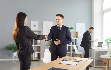 Cheerful businessman shakes hands with a client or coworker during an office meeting, marking an agreement and partnership. Teamwork and deal-making in a professional business setting.の写真素材