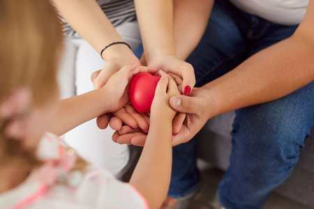 Loving happy friendly family holding red heart in hands close up, showing unity, care, support, promoting charity, donation campaign, health insurance, medical cardiology checkup, peace and hopeの写真素材