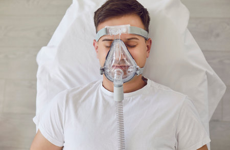 Front view portrait of Caucasian man lying in hospital bed with oxygen mask. Ventilation, sick patient with respiratory equipment for emergency breathing assistance. Close up shot, top view.の写真素材
