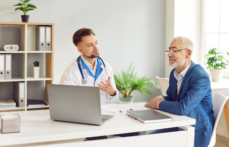 Serious young GP doctor showing laptop screen to old senior male patient, explaining electronic prescription, medical screening, examination result, giving consultation visiting practitioner in clinicの写真素材