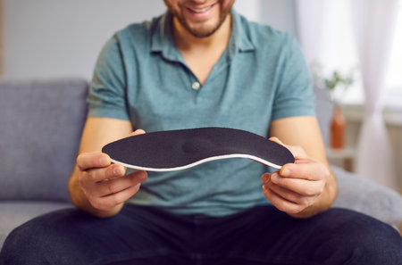 Positive man orthopedist holds a shoe insole in hand, importance of orthotic care for flat feet and foot health. This image highlights medical professionalism and orthopedics expertise.の写真素材