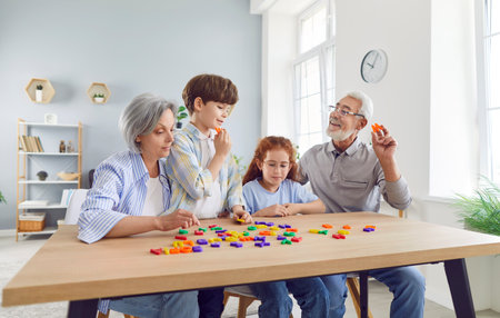 Portrait of cheerful grandfather and grandmother teaching their grandchildren alphabet making words of letters sitting at table. Kids with grandparents playing home. Family leisure concept.の写真素材