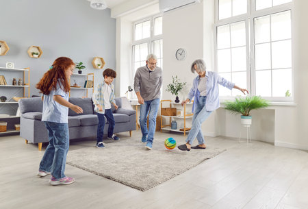 Active seniors, loving elderly grandparents have fun playing ball with little children in living room, happy caring mature engaged in funny game activity with small grandchildren to enjoy weekendsの写真素材