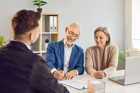 Happy senior couple clients is signing a contract with an real estate agent, financial adviser, or investment consultant in an office. The contract involves insurance and financial matters.の写真素材