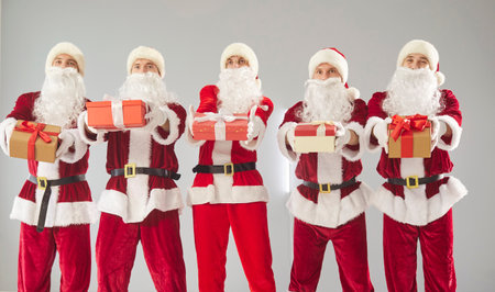 Happy New Year cute group presenting gift box, partying fun wearing Santa Claus holiday costumes, Merry Christmas red suits, celebrating festive season, gathered together enjoying lively joyful partyの写真素材