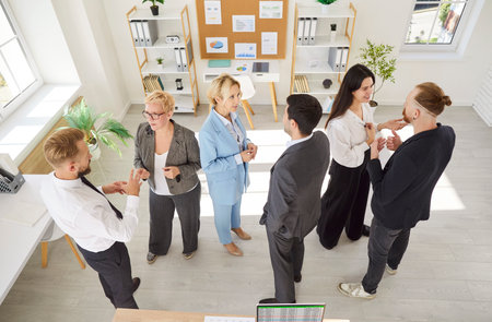 Top view of group of business professionals gathering in modern office engaged in lively discussion in small groups. Male and female colleagues exchanging ideas and sharing opinions during meeting.の写真素材