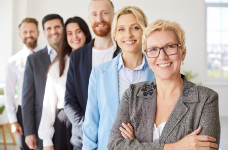 Group of business confident people men and women looking cheerful at camera and smiling indoors. Company employees in formal clothes standing in office in a row. Team work concept.の写真素材