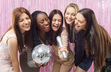 Happy smiling multiracial friends girls karaoke singing, women have fun at hen party at club, diverse female laughing to celebrate bachelorette bridal shower, entertainment gathering before weddingの写真素材