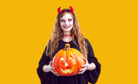Portrait of woman with sly and devious smile who poses with Halloween glowing pumpkin. Cute...