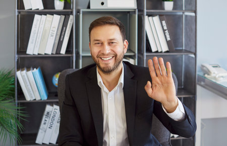 Businessman waving hello, interacting on video call online with friendly gesture and open smile,...