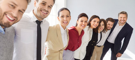 Group portrait of a happy smiling business people standing in a row and hugging isolated on gray...