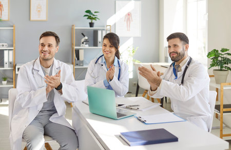Happy smiling doctors rejoicing at success in treatment applauding sitting at desk in clinic during a meeting. Successful team of young medical staff in hospital. Health care concept.の写真素材