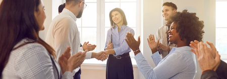 Diverse group of joyful satisfied company employees applauding to celebrate success after work meeting, shaking hands with smiling female colleague or business coach in end of presentation. Banner.の写真素材