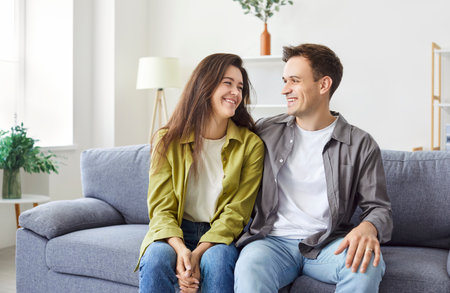 Portrait of young happy married couple sitting together on sofa, hugging and looking at each other. Cheerful smiling young Caucasian man and woman on couch in living room radiating love and happiness.の写真素材
