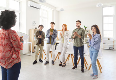 Team of coworkers applauding to businesswoman during a meeting or presentation in the office, celebrating success. Focusing on teamwork, collaboration, and the joy of achieving goals together.の写真素材