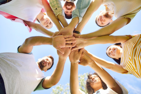 Bottom view of young happy people friends or a group of students gathered together outdoors and putting their arms in a pile on blue sky background. Friendship, unity and teamwork concept.の写真素材